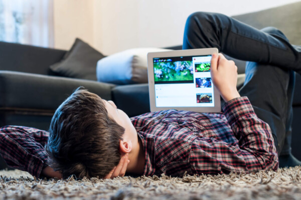 Teenager laying on the floor in the room looking at iPad or tablet