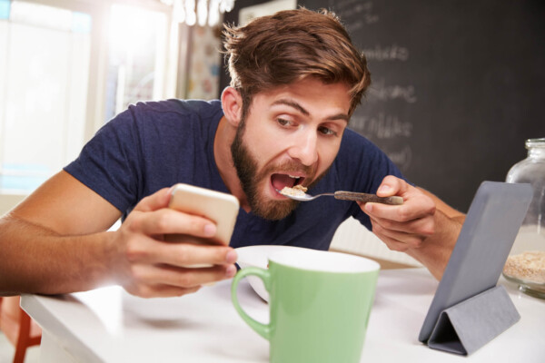 Man eating breakfast while looking at phone, tablet