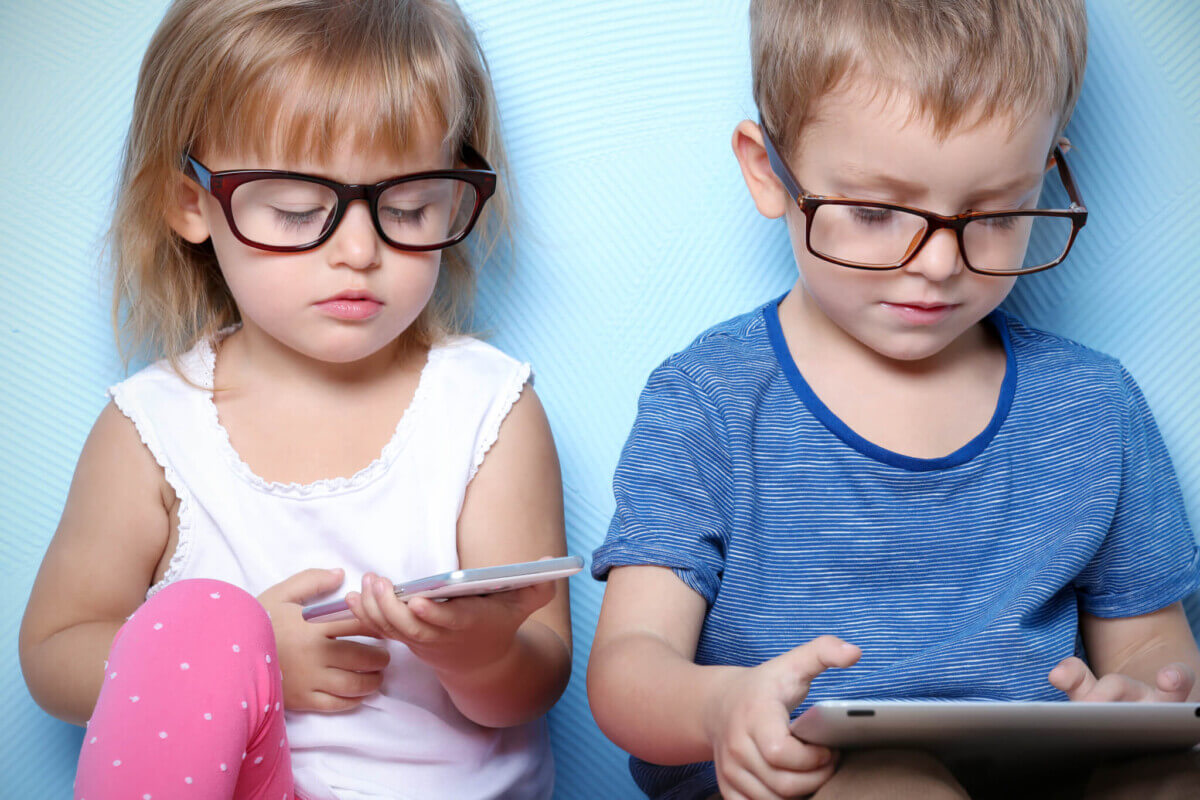 Cute funny children with tablet computer and mobile phone on color background