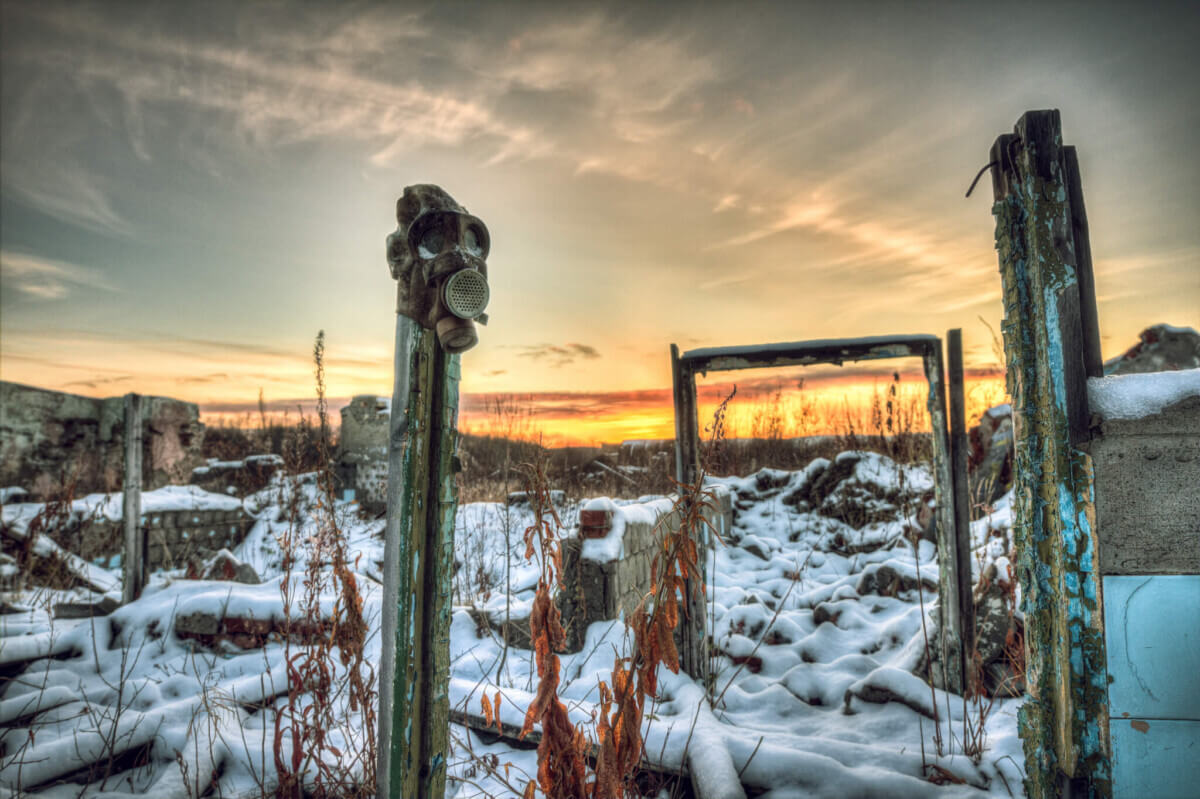 The post-apocalyptic world. Nuclear winter. Old gas mask in the ruins. The remains of houses covered with snow at sunset