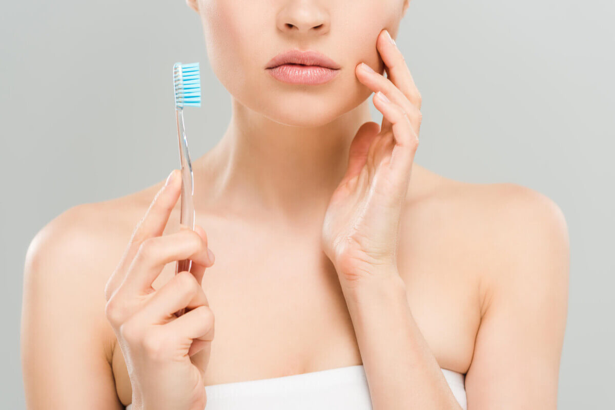 cropped view of woman touching face and holding toothbrush isolated on grey