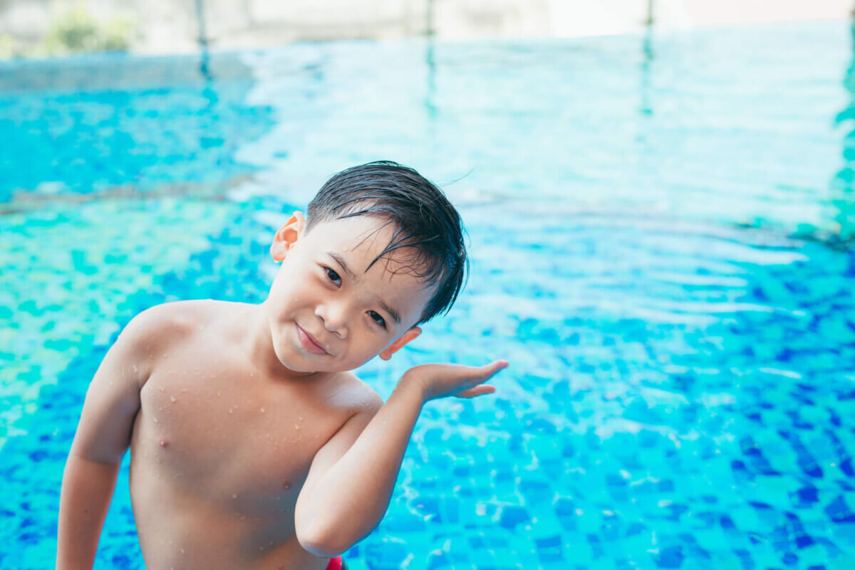 Cute asian kid cleaning ears after swimming in a pool