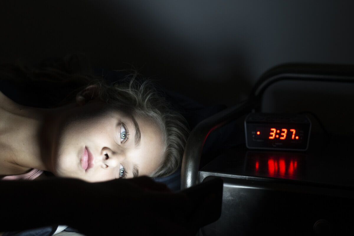Young girl using mobile phone in bed at midnight, can't sleep