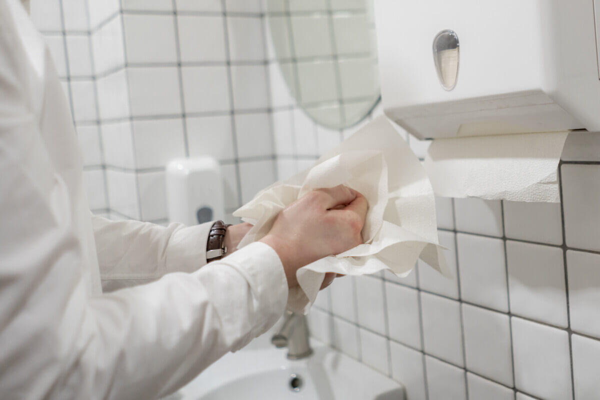 Person using paper towels in office bathroom after washing hands