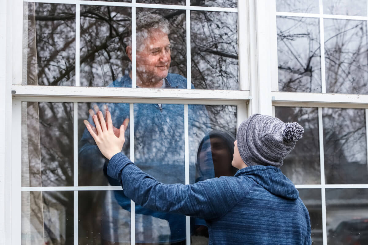 Teen visiting senior citzen quarantined in home, touching hands through the window