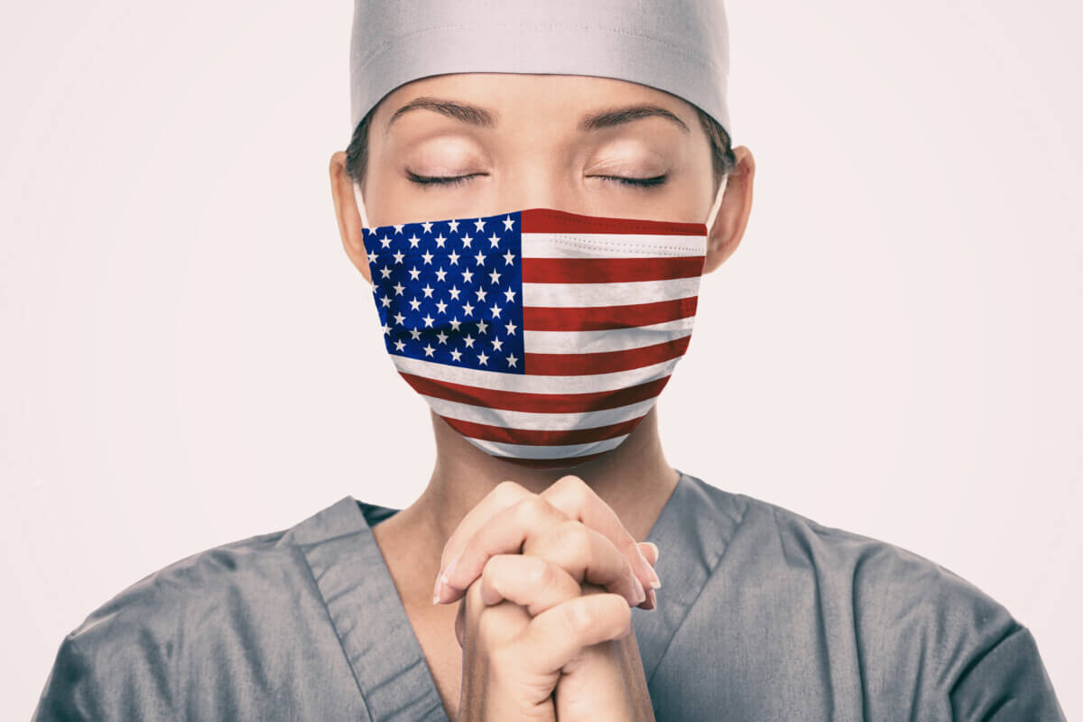 Coronavirus pandemic in the United States of America. USA american flag print on doctor's mask praying with claspeds hands in hope for help. Crying for help, disaster aid needed in the US.