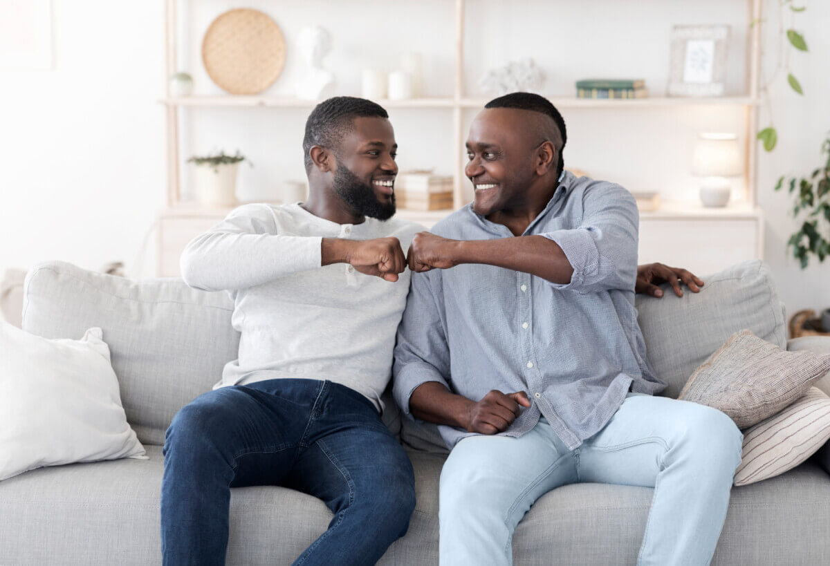 Father-Son Relationships. Adult Black Man And Senior Father Bumping Fists At Home