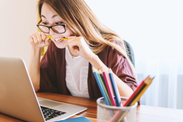 College student stress: Woman biting pencil while doing work on computer