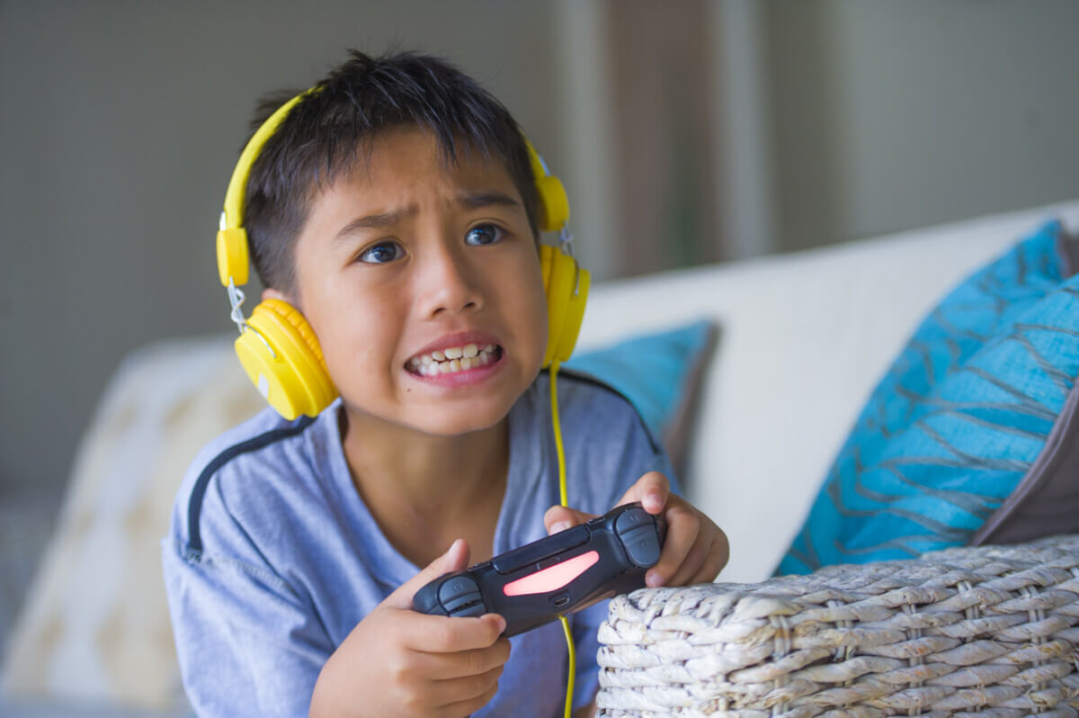 Young child excited and happy playing video game online with headphones holding controller enjoying having fun sitting on couch