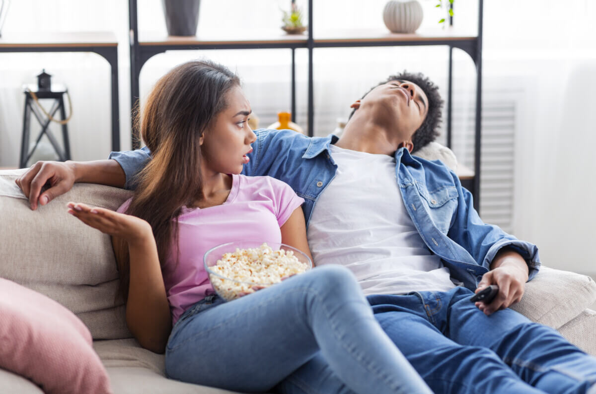 Bored guy sleeping next to girlfriend while watching movie together