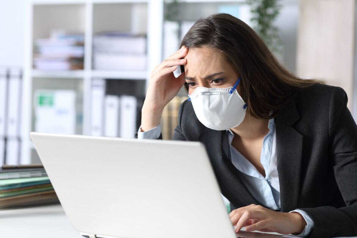 Worried executive with mask reading bad news on laptop