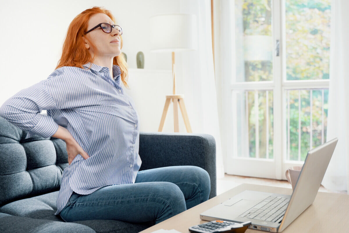 One young redhead woman suffers back pain cramp working at home