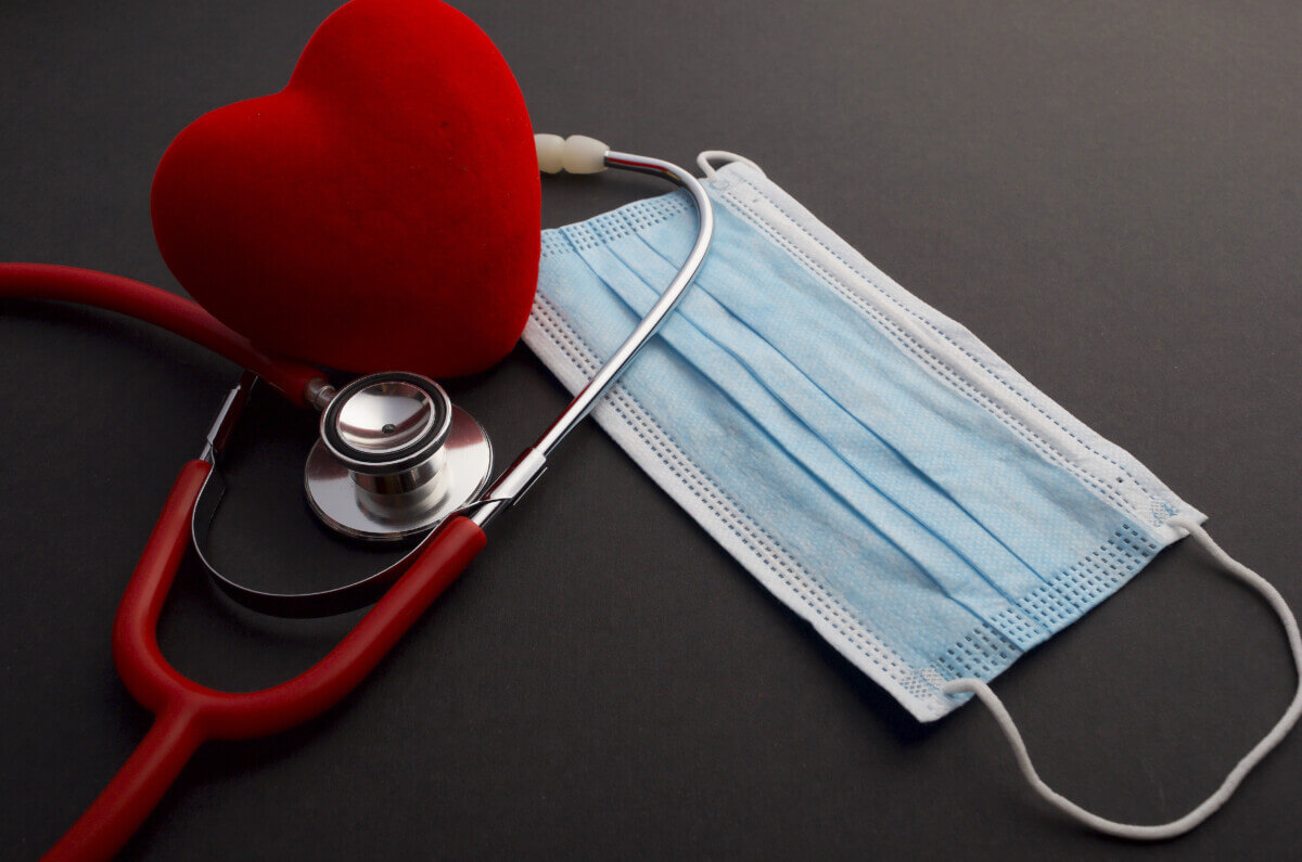 Face mask, red heart and stethoscope on dark background.