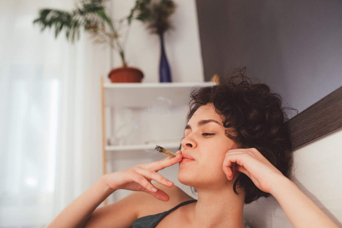 Woman laying on her bed and smoking a marijuana cigarette