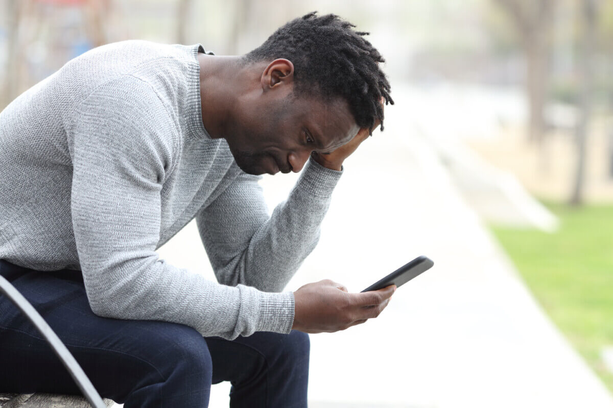 Sad black man checking mobile phone