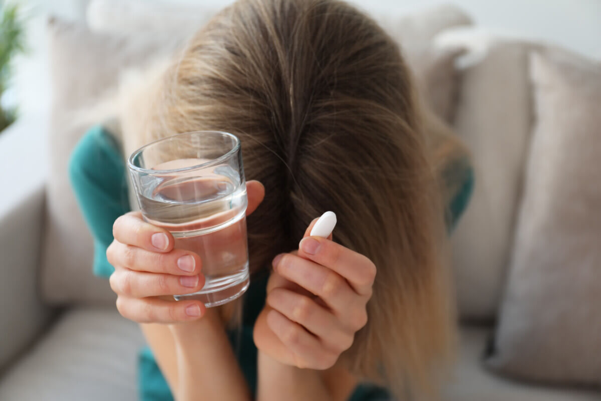 Upset young woman with abortion pill and glass of water at home,