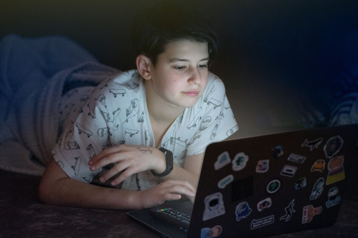 Teenage boy looking at laptop computer in bed at night