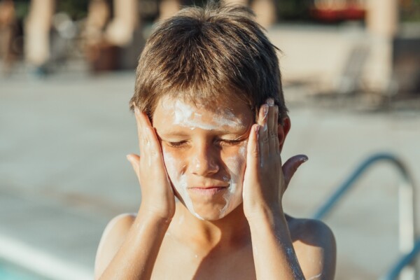 Boy putting sunscreen on his face at the pool