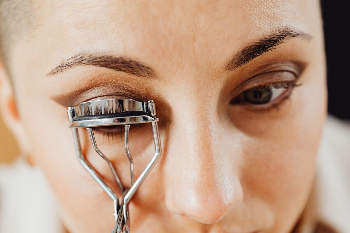 Woman using an eyelash curler while putting on makeup.