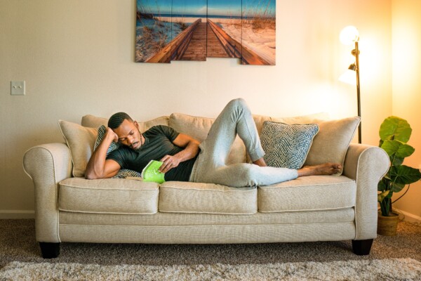Man lying on couch in sweatpants reading a book