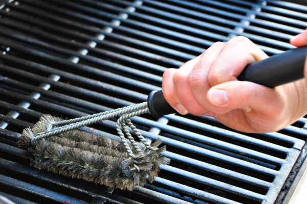 Person using a grill brush to clean their barbecue