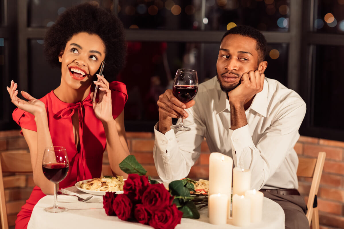Bored man having a horrible date while woman talks on phone at dinner