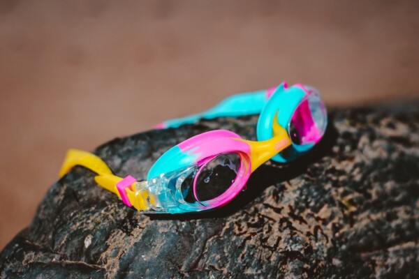 teal and pink swim goggles on a rock