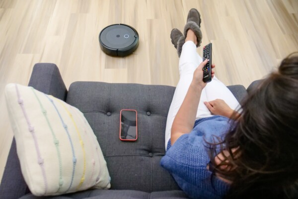 Picture of roomba vacuum on hardwood floor with woman relaxing on couch watching TV