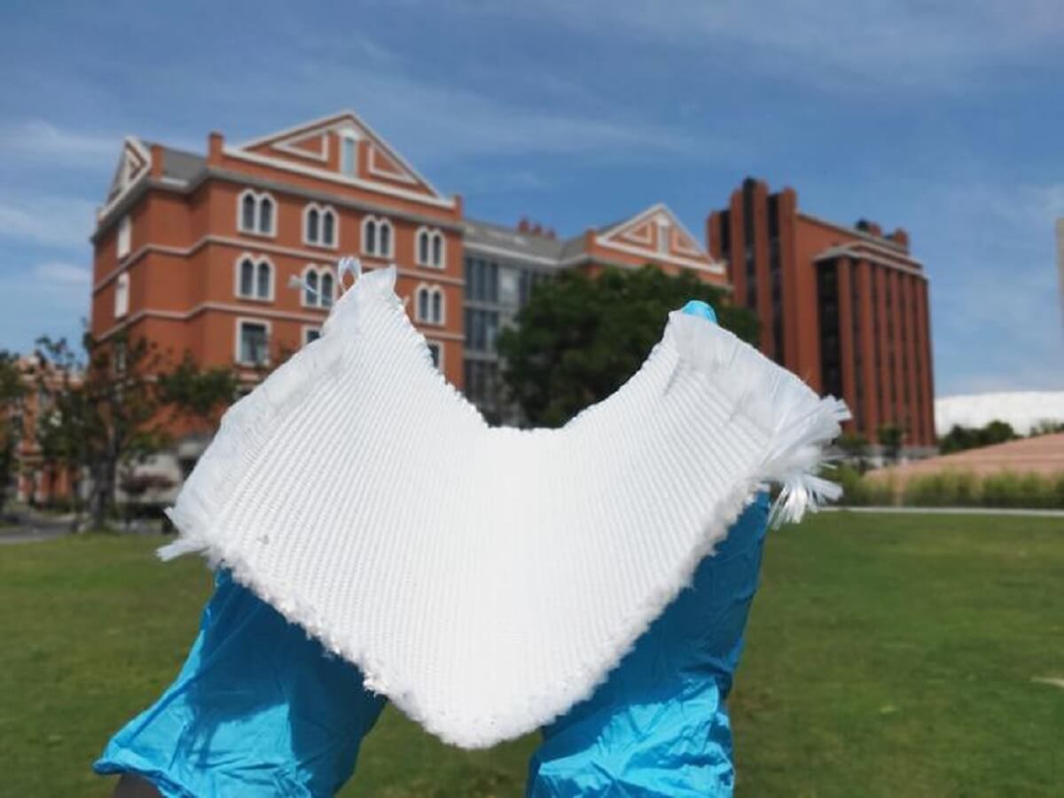  a pair of blue-gloved hands holding a large white fabric, large brown building in the background