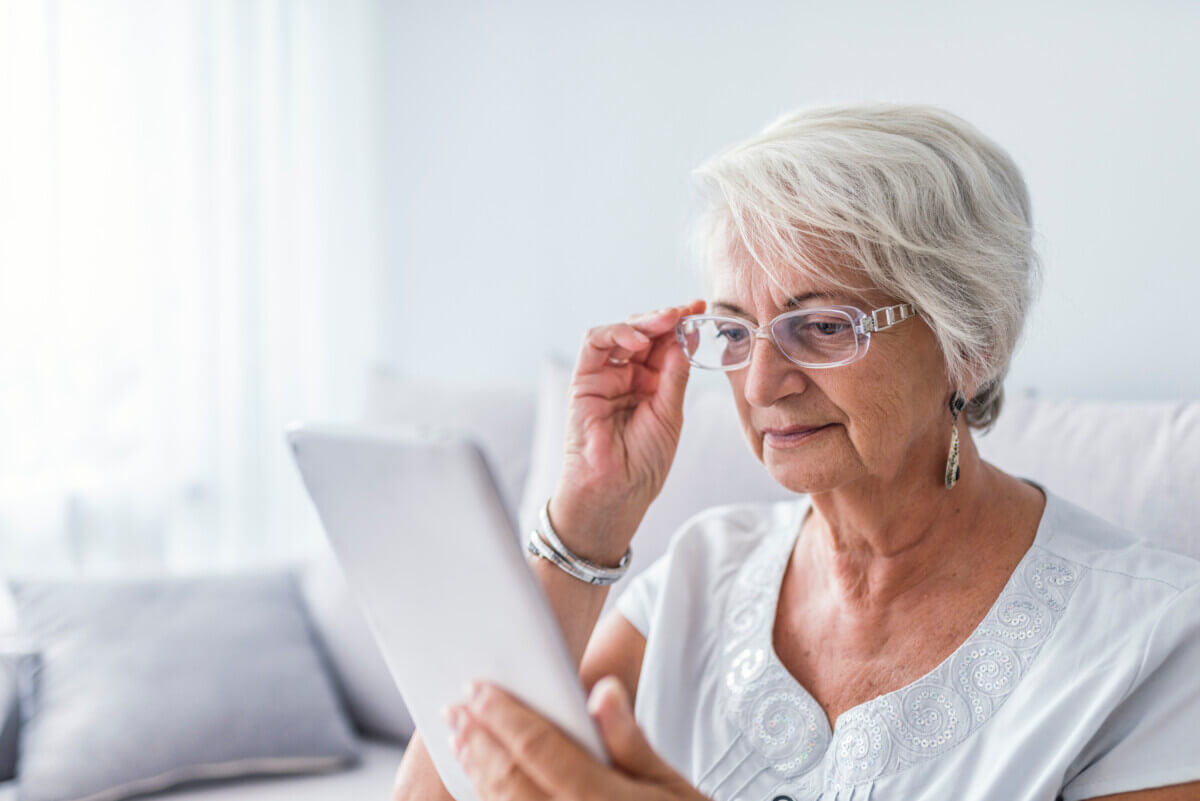 Older woman looking at a tablet while fixing her reading glases