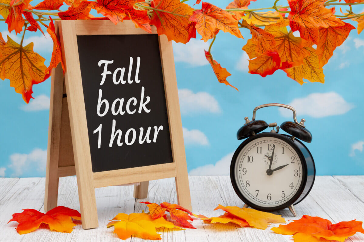 Daylight Saving Time fall back sign with alarm clock on weathered wood with fall leaves