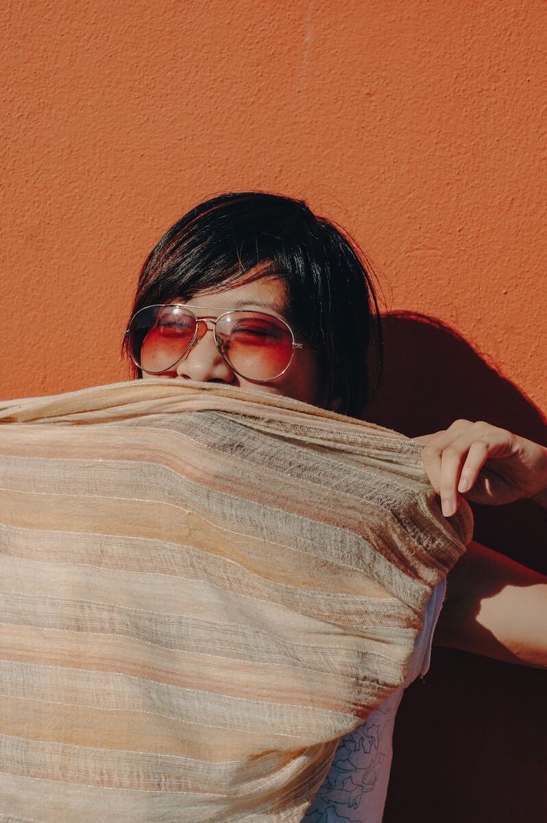 Woman wearing aviator sunglasses covering her face with a blanket