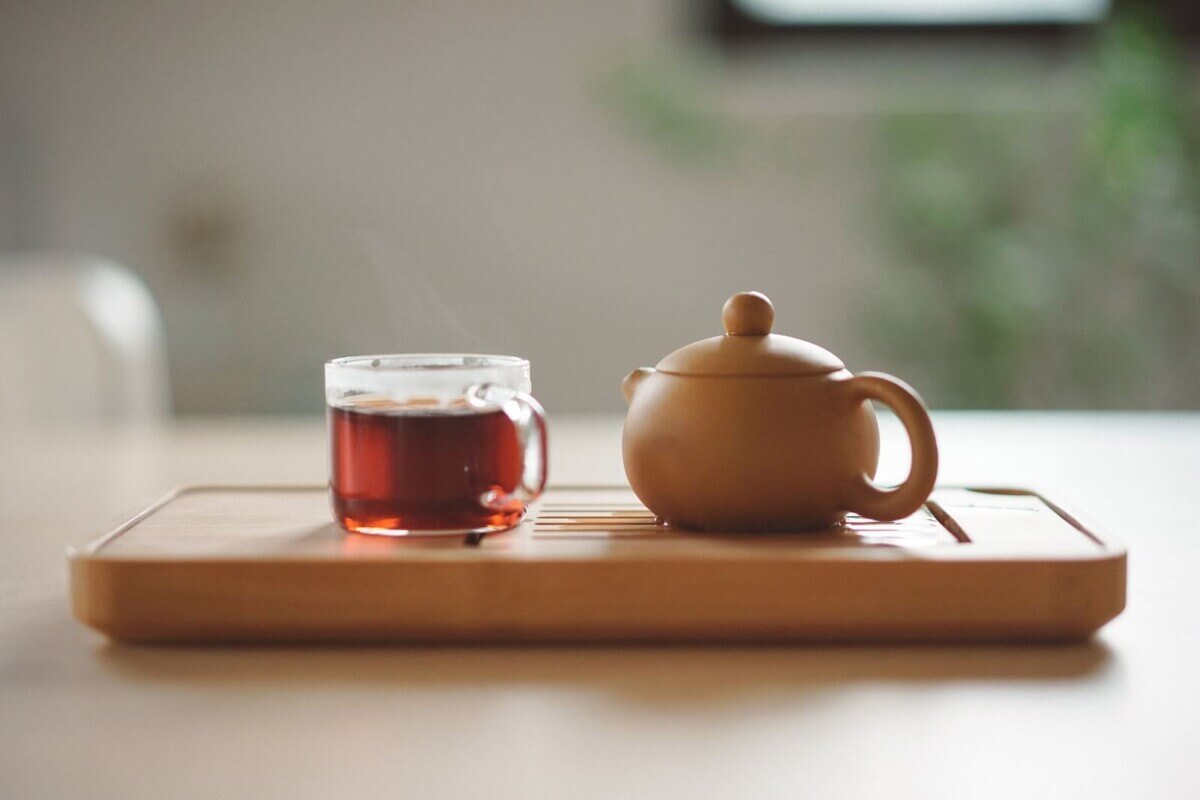 Clear glass cup with turmeric tea near brown ceramic teapot