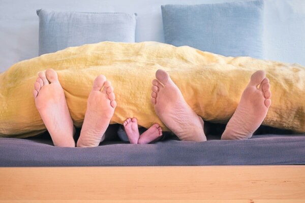 Parents' feet with child's feet sticking out of a bed