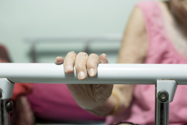 An elderly woman using a bed rail for support