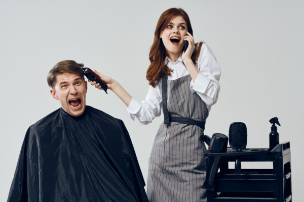 Hairdresser talking on the phone distracted from the haircut while man screams