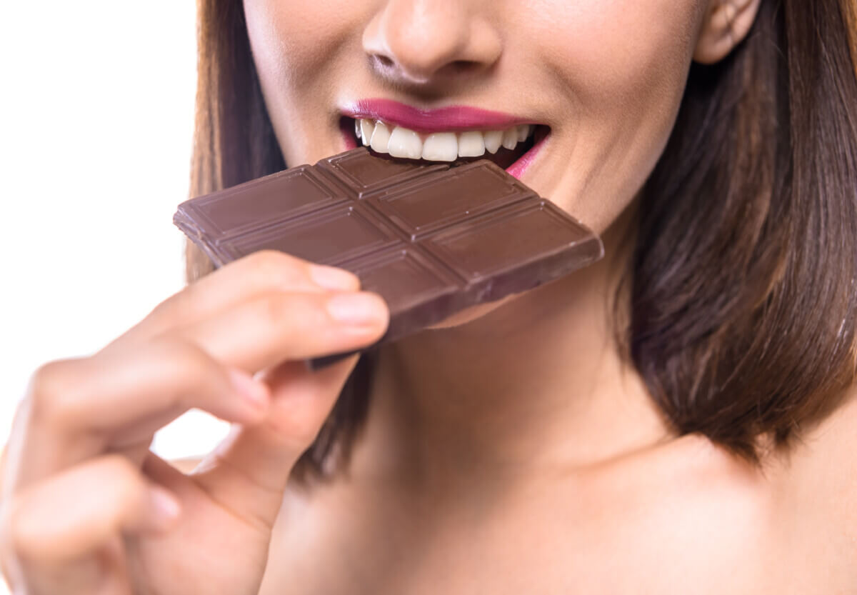 Young woman eating bar of dark chocolate.