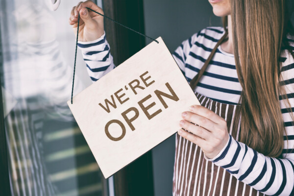 Woman holds the wooden sign with text: we're Open