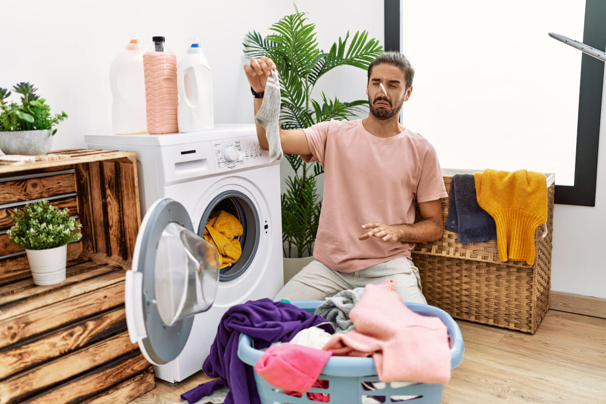 man doing laundry covering nose for smelly sock at laundry room